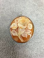 Front view of oval shell cameo showing floral carving and silver bezel