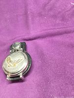 Front view showing metal case with gold eagle emblem and leather backing