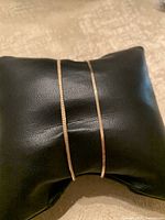 Two flat gold chain bracelets displayed on black cushion