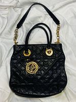 Front view of black quilted Metrocity handbag displaying quilt pattern, handles, chain strap, gold hardware, logo medallion