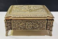 front view of brass jewelry box showing floral relief and feet