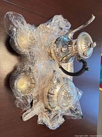 Full view of five-piece silver-plated set on tray, wrapped in plastic