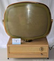 Front view of television showing oval screen in brass-tone frame atop woodgrain cabinet
