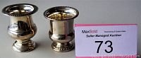 Photo showing two small sterling silver ornate containers side by side, each about 3 to 3.5 inches tall, with polished finish and detailed rims and bases.