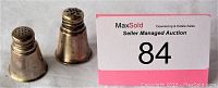 Pair of sterling silver salt and pepper shakers with perforated tops and manufacturer marks on the base shown on a flat surface alongside the auction lot number.