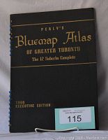Black cover of the atlas with gold embossed title reading 'Perly's Bluemap Atlas of Greater Toronto The 12 Suburbs Complete 1950 Executive Edition'. Spiral binding with some blue clips.