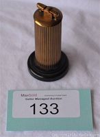 Front view showing bronze-gold vertically ridged cylindrical lighter with black base and MaxSold auction tag.