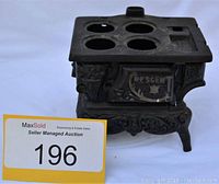 Photo of cast iron toy stove marked with 'PESCEMENT' on front door, showing decorative details and four burner holes on top.