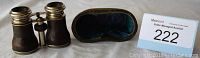 Vintage black textured binoculars with silver metal trim displayed with worn leather case with blue velvet lining.