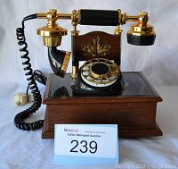 Full front view of decorative rotary phone on wooden base with gold-tone maple leaf decoration, handset, rotary dial, and coiled cord.