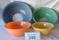Four nesting Pyrex Corning bowls in blue, green, orange, and yellow shown from front angle.