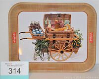 Rectangular metal Coca-Cola serving tray with a rustic picnic basket and Coca-Cola bottles illustration, with Coca-Cola logos on either side and a basket-weave border pattern.