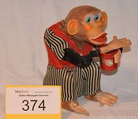 Photo of a vintage mechanical clapping monkey toy with striped pants and a red vest, holding a red bucket with dice graphics.