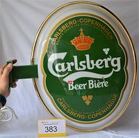 Oval green Carlsberg Beer light-up sign with crown logo and yellow edge, held by hand to show size, photo includes auction lot card 383.