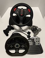 Two steering wheels, pedal unit, DualShock controllers and accessory grips visible