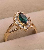 Close-up of ring showcasing green center stone and clear halo stones in gold-tone setting