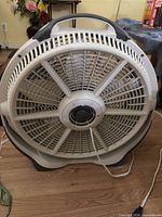Front view of circular floor fan showing grille, carry handle, cord