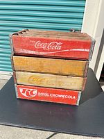 Stack of four branded and unbranded wooden soda crates showing side logos and wear
