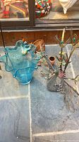 Metal peacock sculpture alongside blue art glass vase on stone floor