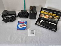 Group shot of all items: Vivitar camera in case, Tasco binoculars, box camera with film canister, sealed Polaroid 600 film