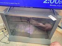 Front view of gray TV stand with glass doors, TV on top (not included)