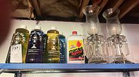 Shelf with two etched glass electric luster lamps and several bottles of lamp oil and lighter fluid