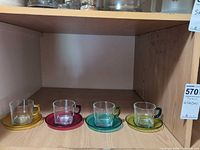Four coloured glass cup and saucer sets displayed on shelf