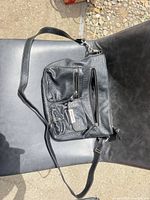 Full view of Rosetti black faux leather crossbody bag on chair showing overall design and strap