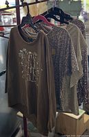 Four tops on hangers showing variety of prints and metallic finishes