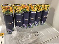 six Van Gogh printed tubes standing upright with bubble-wrapped flute on shelf