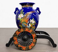 Vase seated on decorative cart, front view showing peacock design and cart wheel pattern