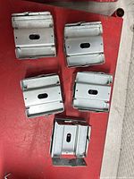 Five galvanized steel post base pieces on red surface