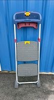 Stool folded showing two grey steps, blue tray top, red hinge parts, yellow latch