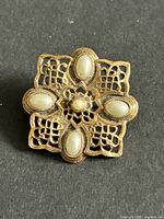 Front of gold tone brooch showing filigree pattern and five faux pearls