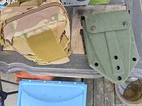 Camouflage pouch and green shovel sheath on table
