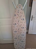 Front view of ironing board standing upright with floral cover visible