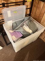 Clear plastic bin open showing contents including grey bag and packaged shirt