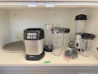 Overall view showing Ninja base, Hamilton Beach base with jar, multiple cups, lids, blades