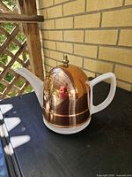 Full view of teapot showing porcelain body, copper-plated lid, brass knob