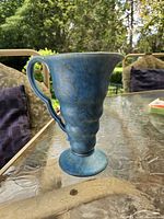 Front view of blue-turquoise ceramic pitcher showing handle, scalloped rim and footed base