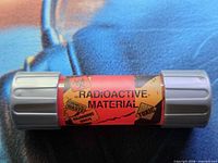 Side view of ooze canister showing red-orange “Radioactive Material” label and gray ribbed end caps