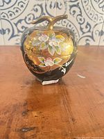 Apple-shaped black and gold floral glass trinket jar with lid in place