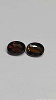 Two oval faceted orange tourmaline gemstones on white background