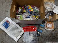 Open box showing mixed lot: door knob sets, electrical parts, braided hose plus separate register and power cord packages