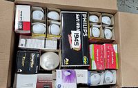 Top view of open box showing multiple boxed and loose incandescent bulbs of various brands and wattages