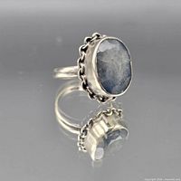 Side view of ring showing oval faceted blue stone and bezel with chain border