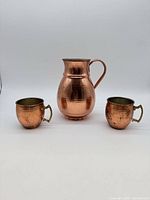 Front view of hammered copper pitcher flanked by two mugs