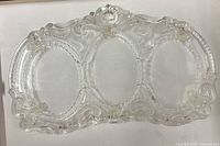 Front view of clear pressed glass frame showing three oval openings and ornate scrollwork