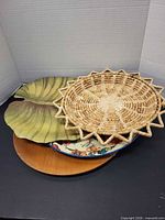 Stack of four trays showing wicker basket on top, green leaf tray, metal floral tray, and wood tray edge