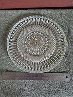 Top view of clear pressed glass platter showing starburst and diamond pattern with ruler for scale